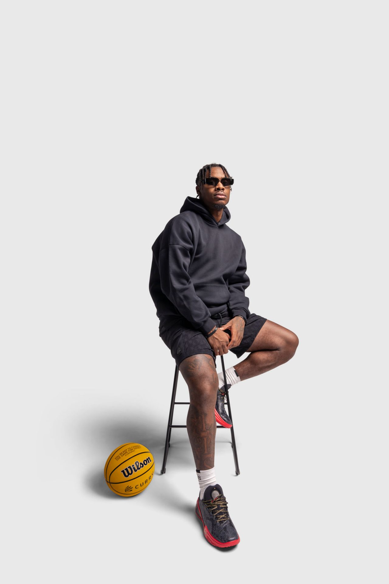 Davion sitting on a stool in a black hoodie and sunglasses with a basketball n the floor