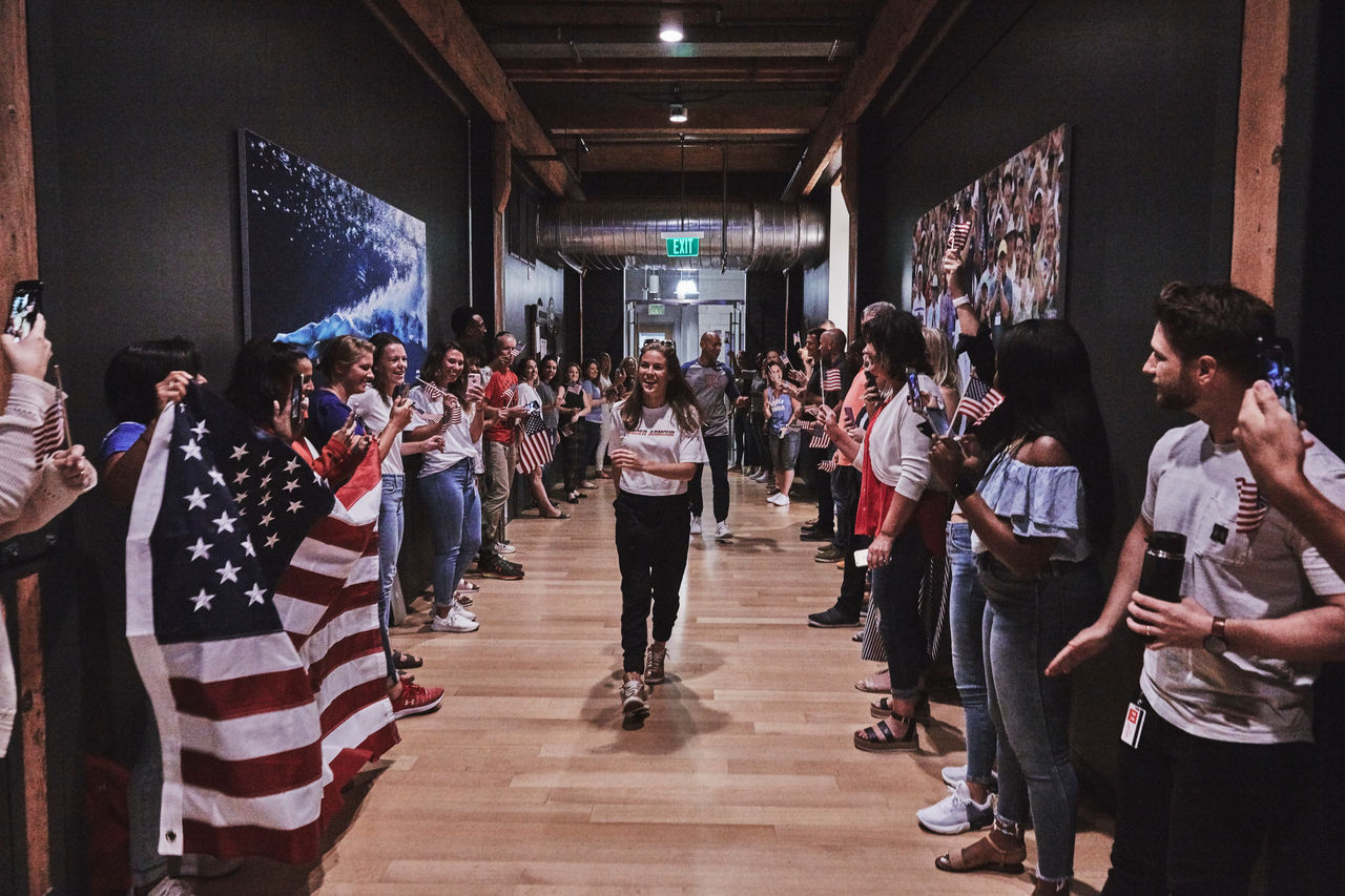 Kelley O’Hara posant vêtue d’un bonnet Under Armour orange et d’une veste zippée grise Under Armour