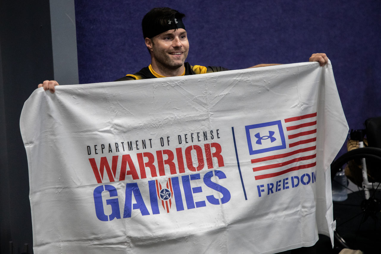 Un homme tenant un drapeau sur lequel est écrit « Warrior Games »